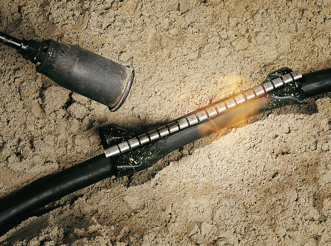 Ein heißer Luftbrenner wird verwendet, um ein Schrumpfschlauch-Verbindungselement auf einem Kabel zu befestigen, das im Sand liegt.