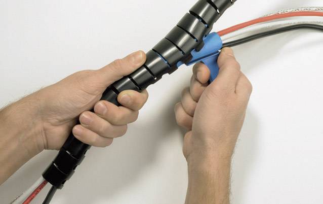 Zwei Hände nutzen ein blaues Werkzeug, um Kabel in einem schwarzen Kabelschutz zu organisieren.