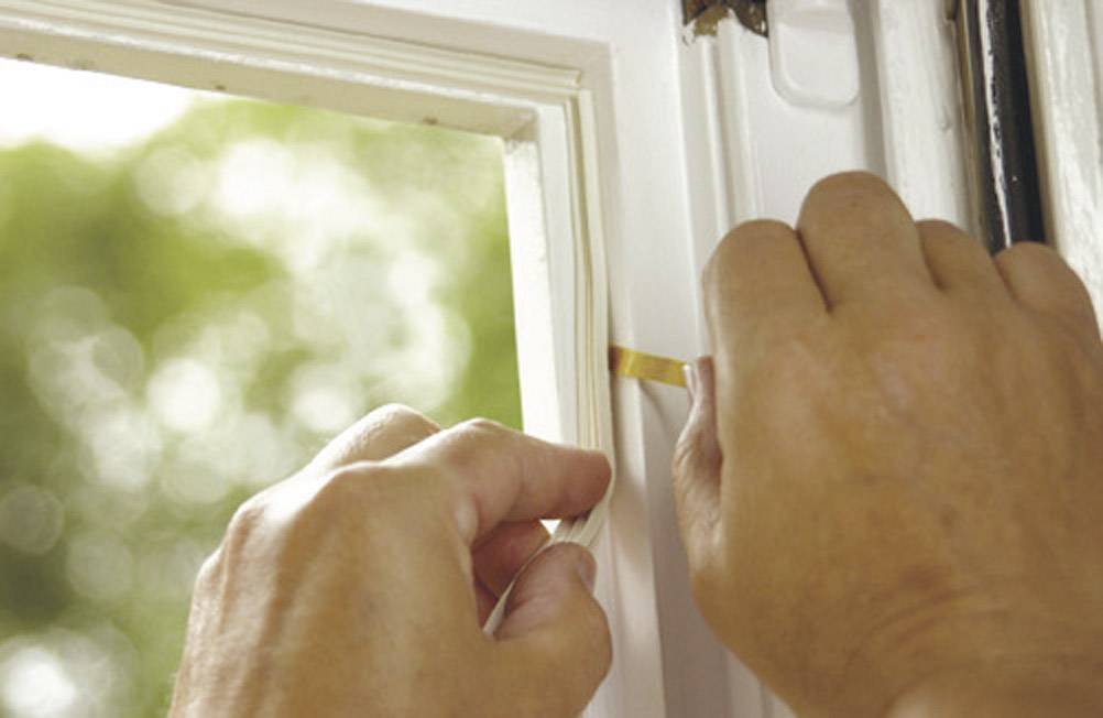 Hände kleben Dichtungsstreifen an Fensterrahmen zur Verbesserung der Isolation.