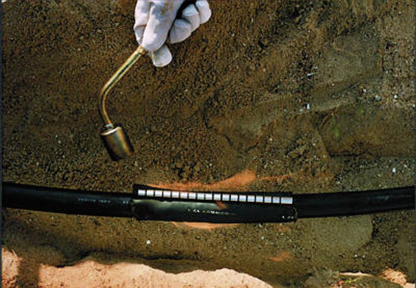 Eine Person testet die Dichtheit einer unterirdischen Pipeline mit einem Hammer auf einer sandigen Oberfläche.