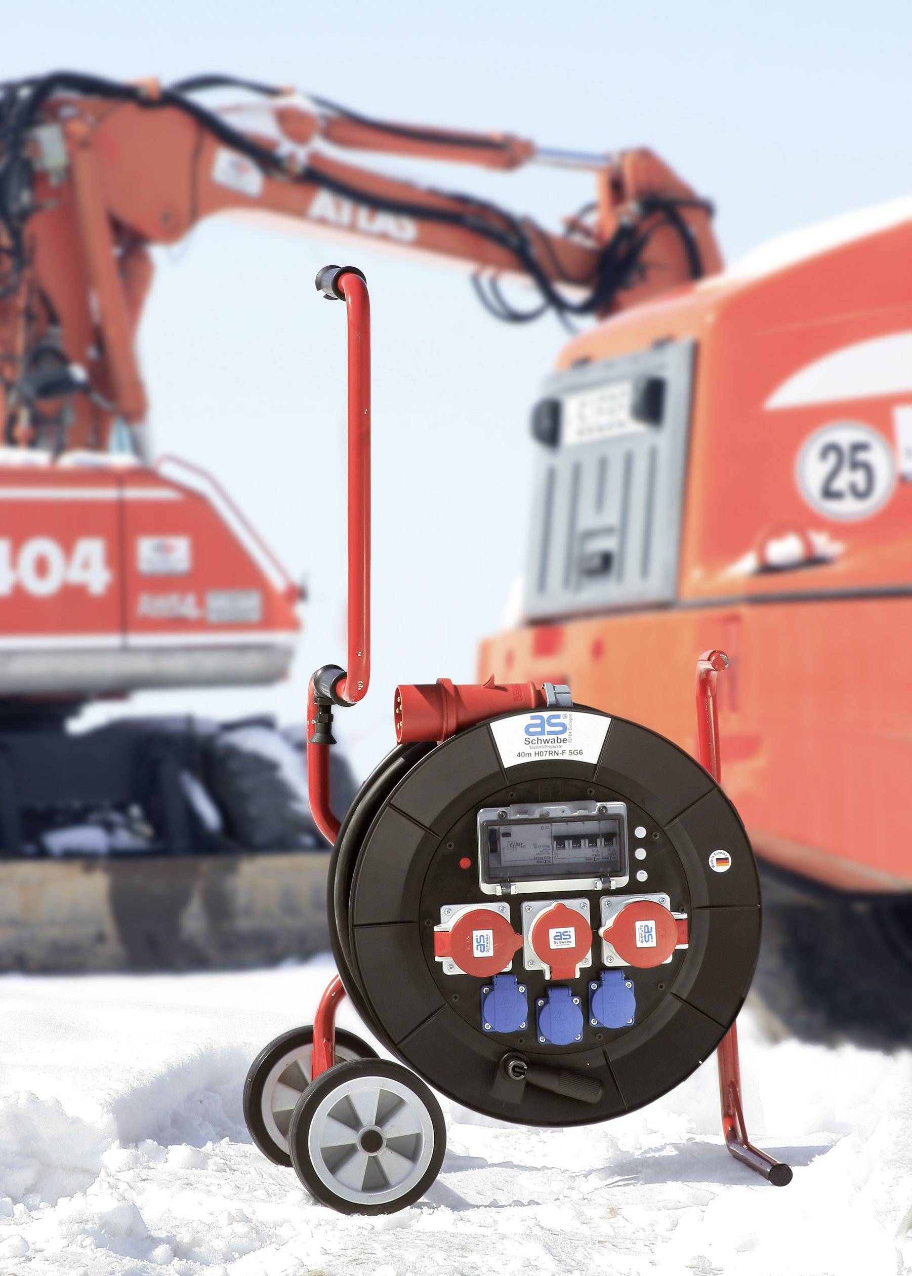 Ein rote Kabeltrommel mit mehreren Steckdosen im Schnee vor Baumaschinen.
