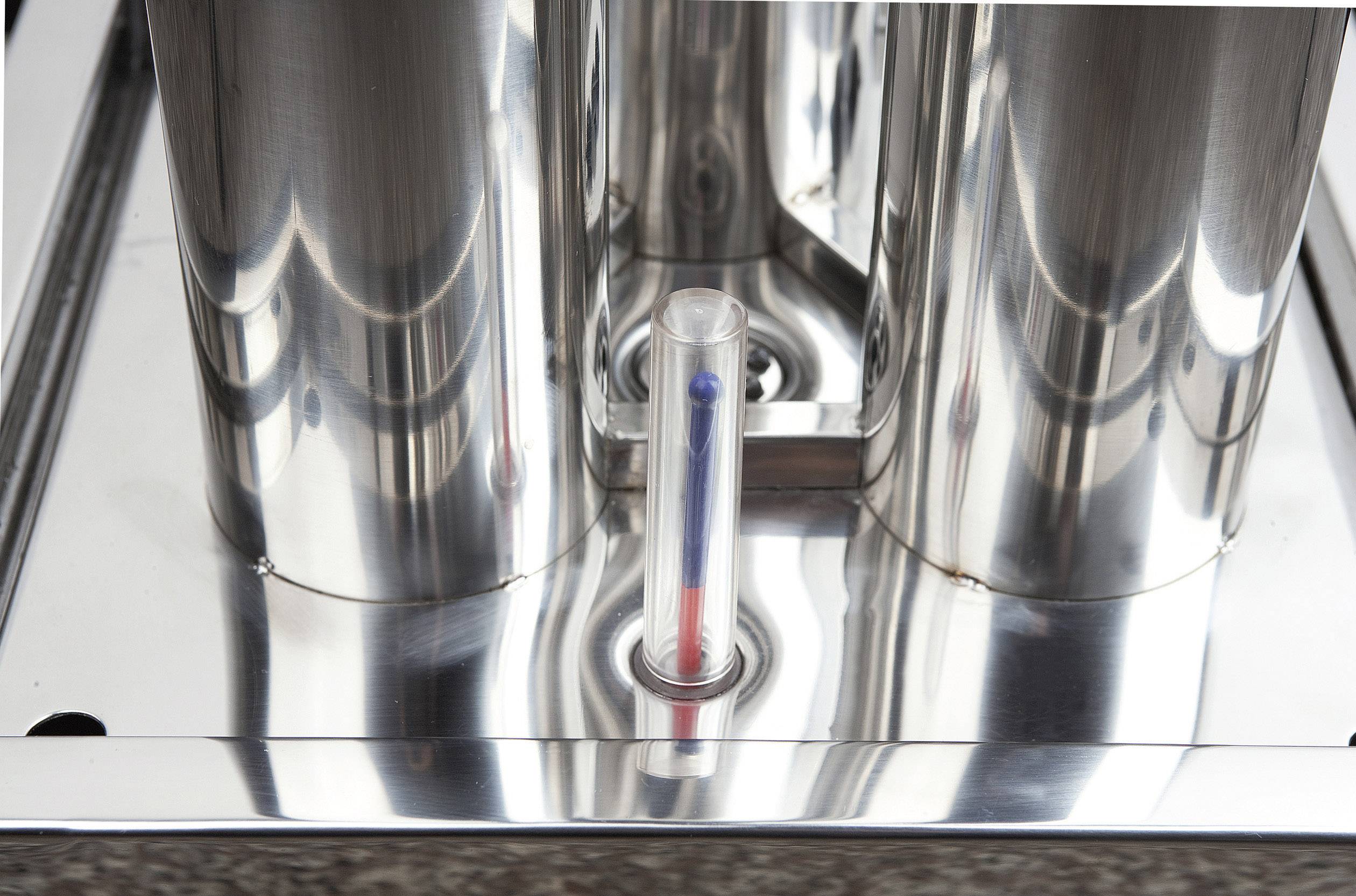 Ein Thermometer misst die Temperatur zwischen zwei glänzenden Metallzylindern. Die Flüssigkeit im Thermometer ist rot und blau.