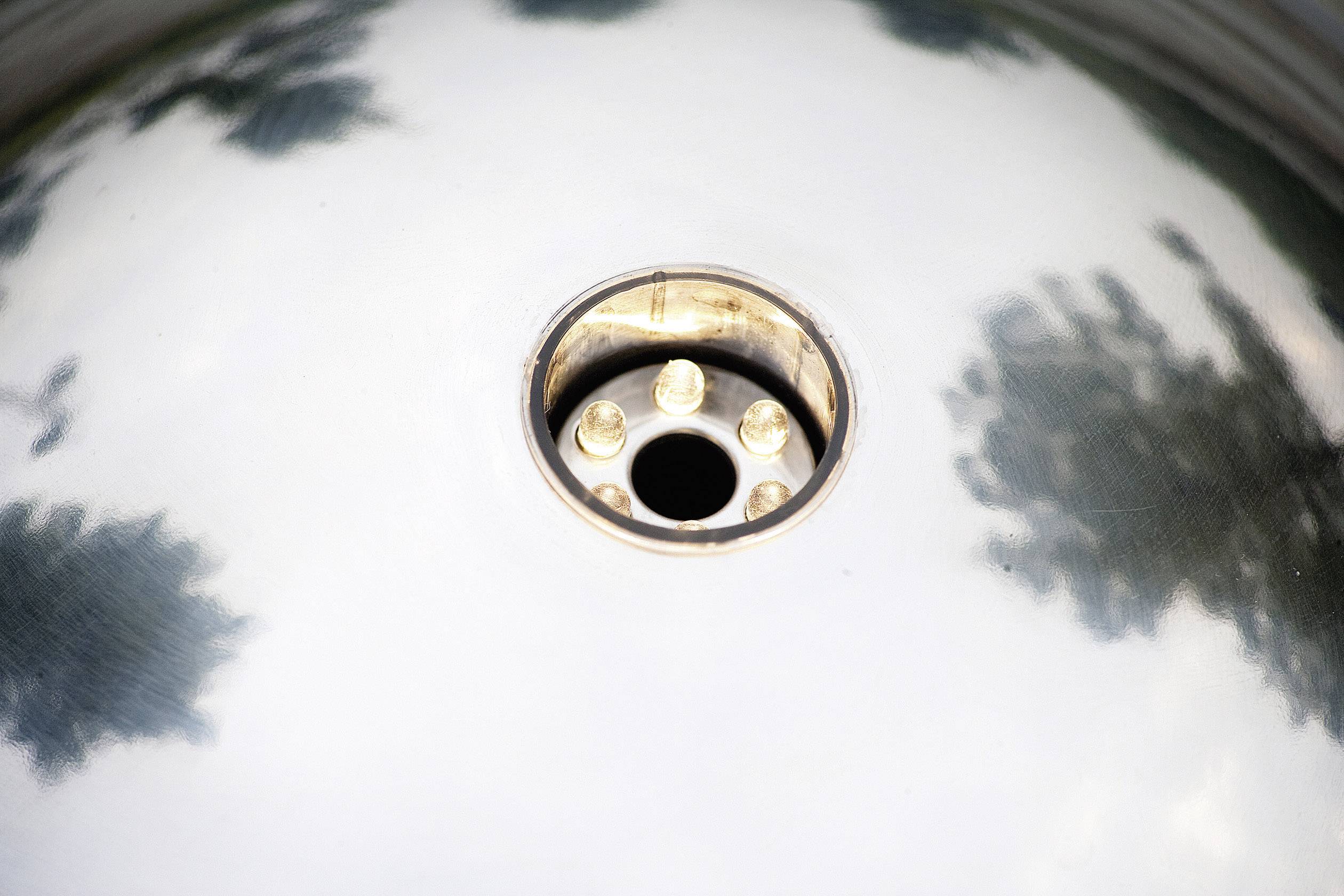 Ein rundes Metallobjekt mit zentraler vertiefter Öffnung, umgeben von Bäumen, die sich auf der polierten Oberfläche spiegeln.