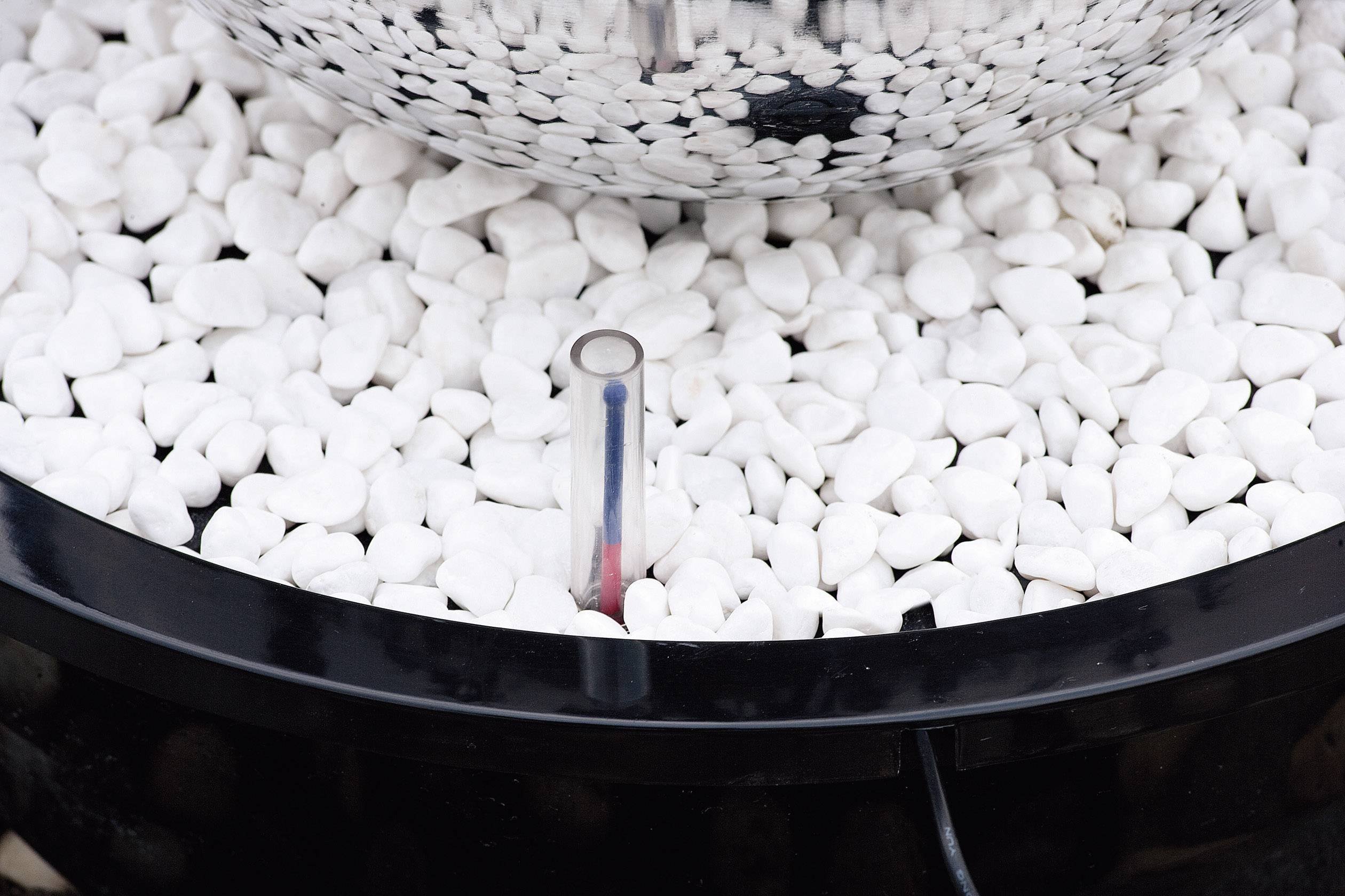 Ein runder Metallbehälter auf weißem Kies mit einem kleinen Thermometer, das die Temperatur der Umgebung misst.