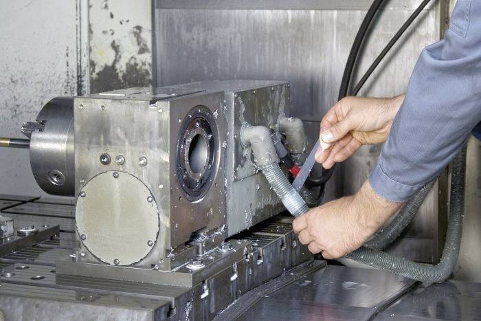 Eine Person in Arbeitskleidung montiert oder überprüft Schläuche an einer industriellen Maschine in einer Werkstattumgebung.