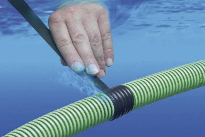 Eine Hand benutzt ein schwarzes Reparaturband, um ein grün-weiß gestreiftes Rohr unter Wasser abzudichten.