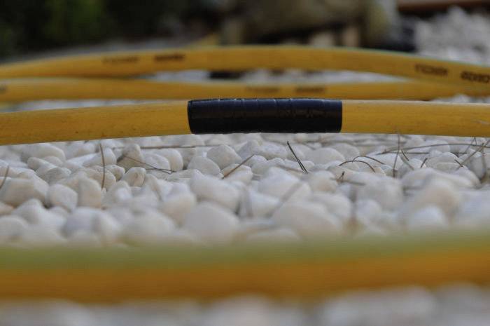 Ein gelber Gartenschlauch liegt auf weißen Kieselsteinen. Der Schlauch hat einen schwarzen Abschnitt. Hintergrund leicht verschwommen.