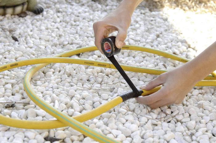 Eine Person befestigt einen gelben Gartenschlauch mit schwarzem Klebeband auf einem Kiesboden.