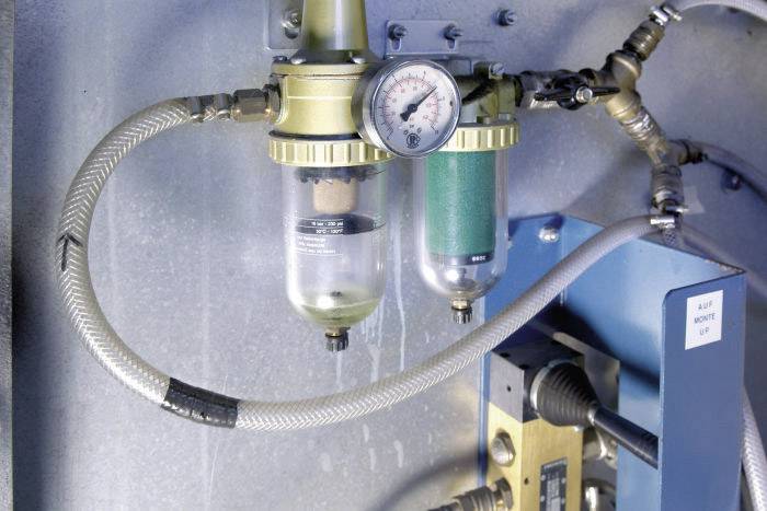 Ein Druckluftregler mit Manometer und zwei Filtern in einem technischen Umfeld. Kabel und Schläuche sind angeschlossen.