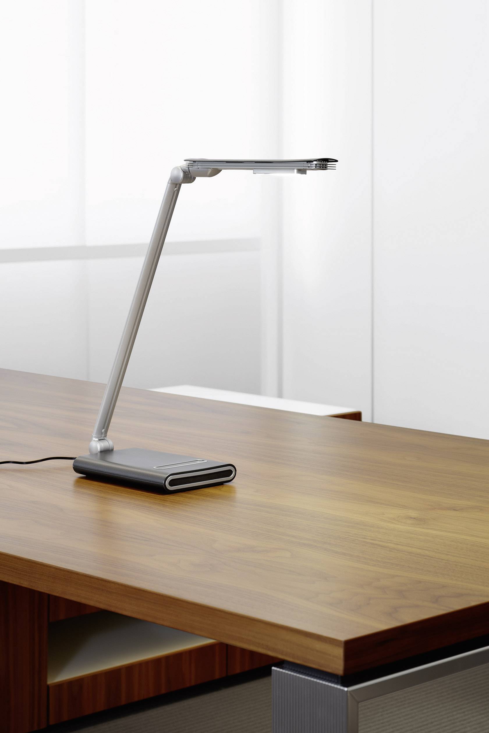 Eine moderne, schlanke Tischlampe steht eingeschaltet auf einem Holztisch vor einem neutralen Hintergrund.