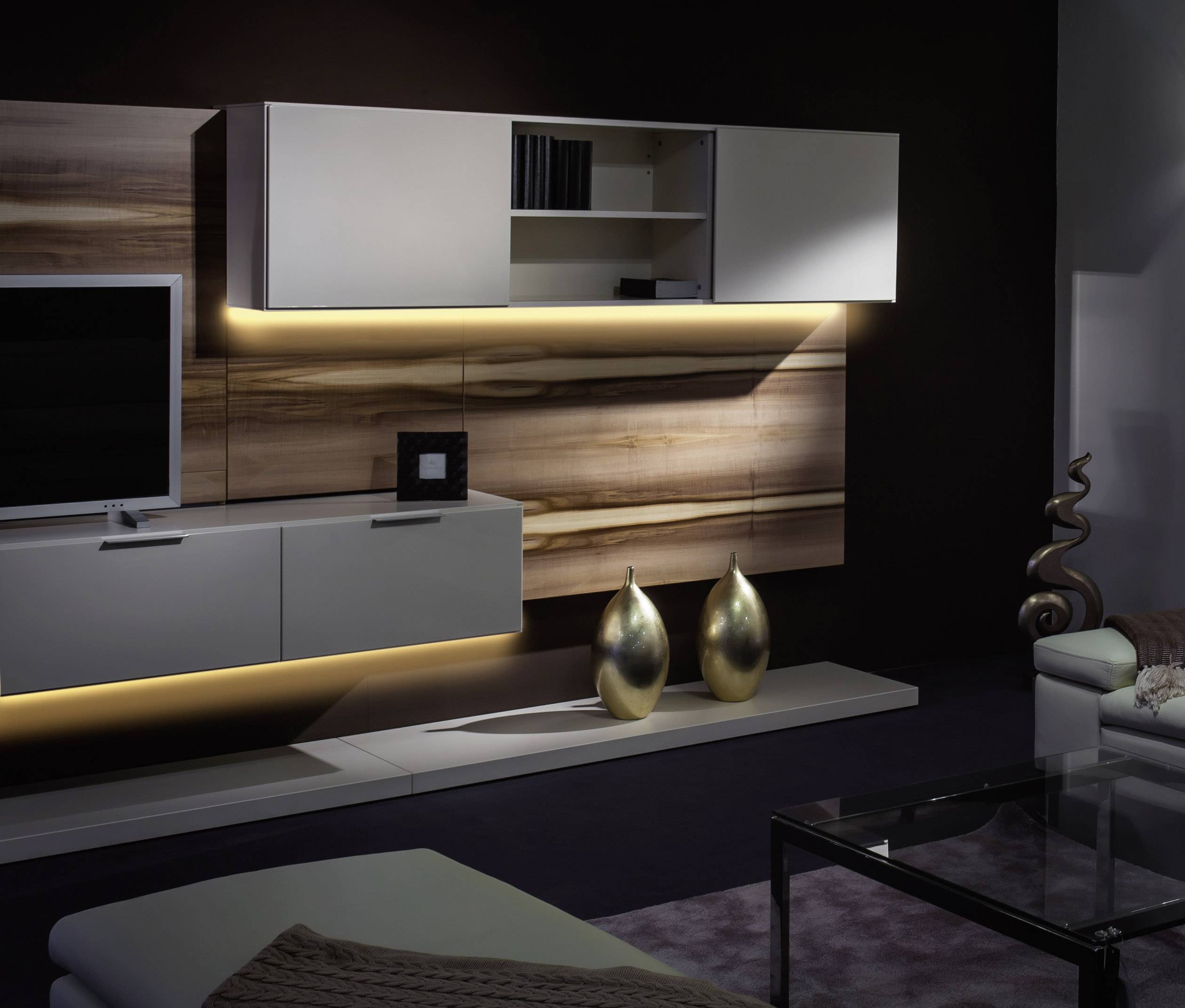 Wohnzimmer mit modernem, beleuchtetem Wandschrank in Holzoptik, Fernseher, Glasvase, Dekogegenständen und elegantem Sofa.