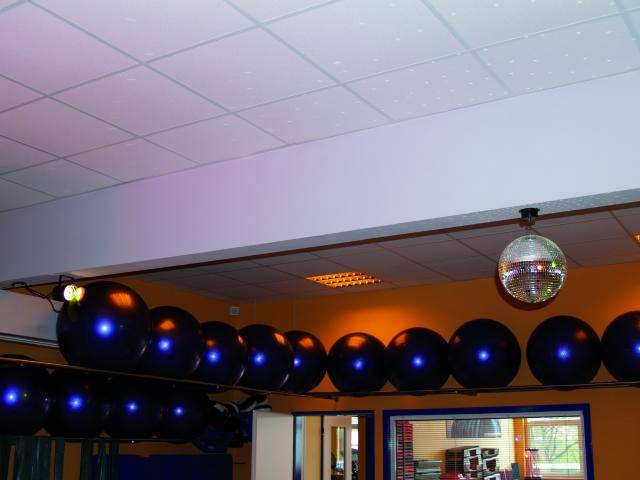 Ein bunt erleuchteter Raum mit Gymnastikbällen entlang der Decke und einer Discokugel in der Mitte; sportliche Atmosphäre.