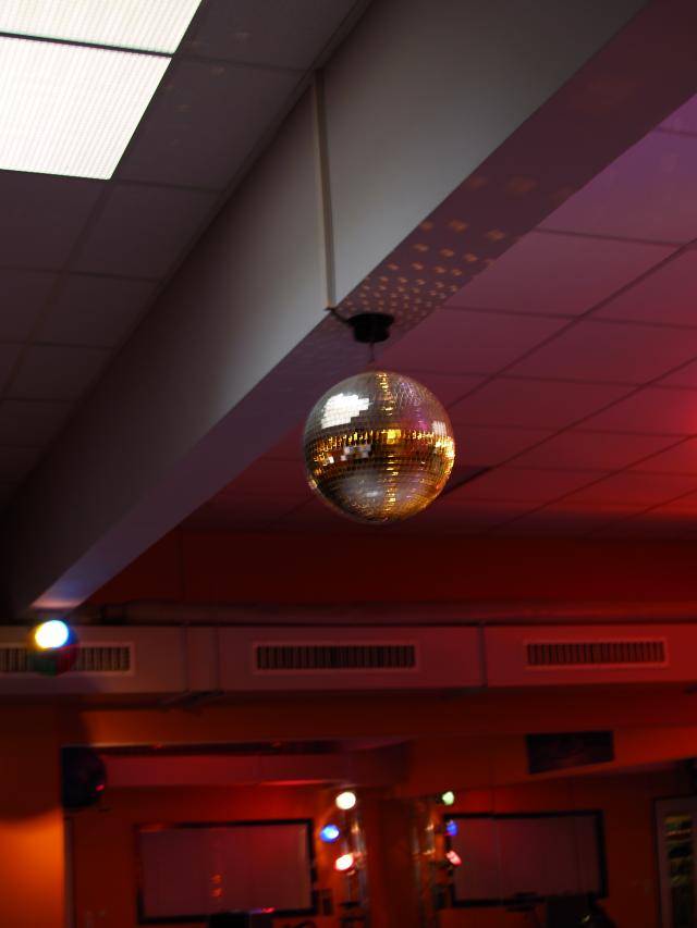 Diskokugel hängt an der Decke eines rot beleuchteten Raumes, reflektiert Lichtpunkte an die Wände. Stimmung von Spaß und Tanz.