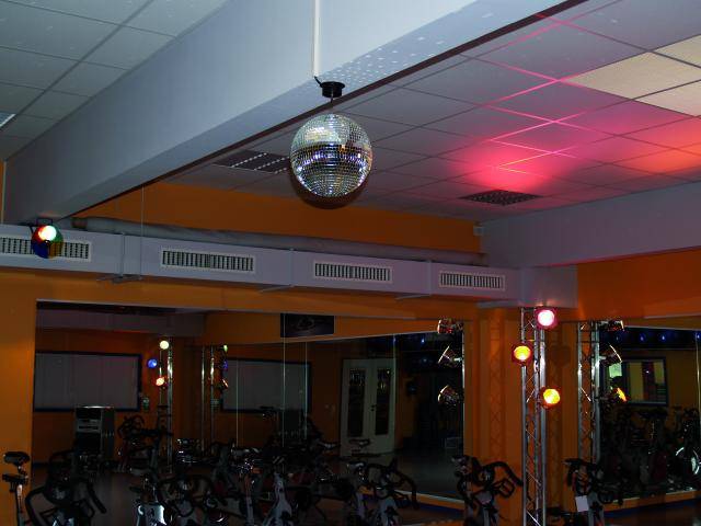 Spinning-Saal mit Spiegelkugel, bunter Beleuchtung und mehreren Spinning-Bikes. Atmosphärische Einrichtung für Musik und Bewegung.