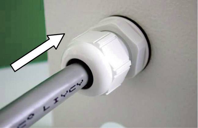 Ein graues Kabel wird durch eine weiße Dichtung in eine Wand geführt. Ein Pfeil zeigt die Richtung des Kabels an.