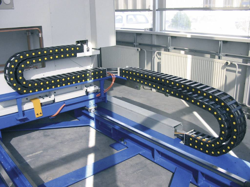 Kabelschleppsystem in einem industriellen Umfeld, zeigt eine Anordnung von zwei schwarzen, flexiblen Trägerketten mit gelben Punkten.