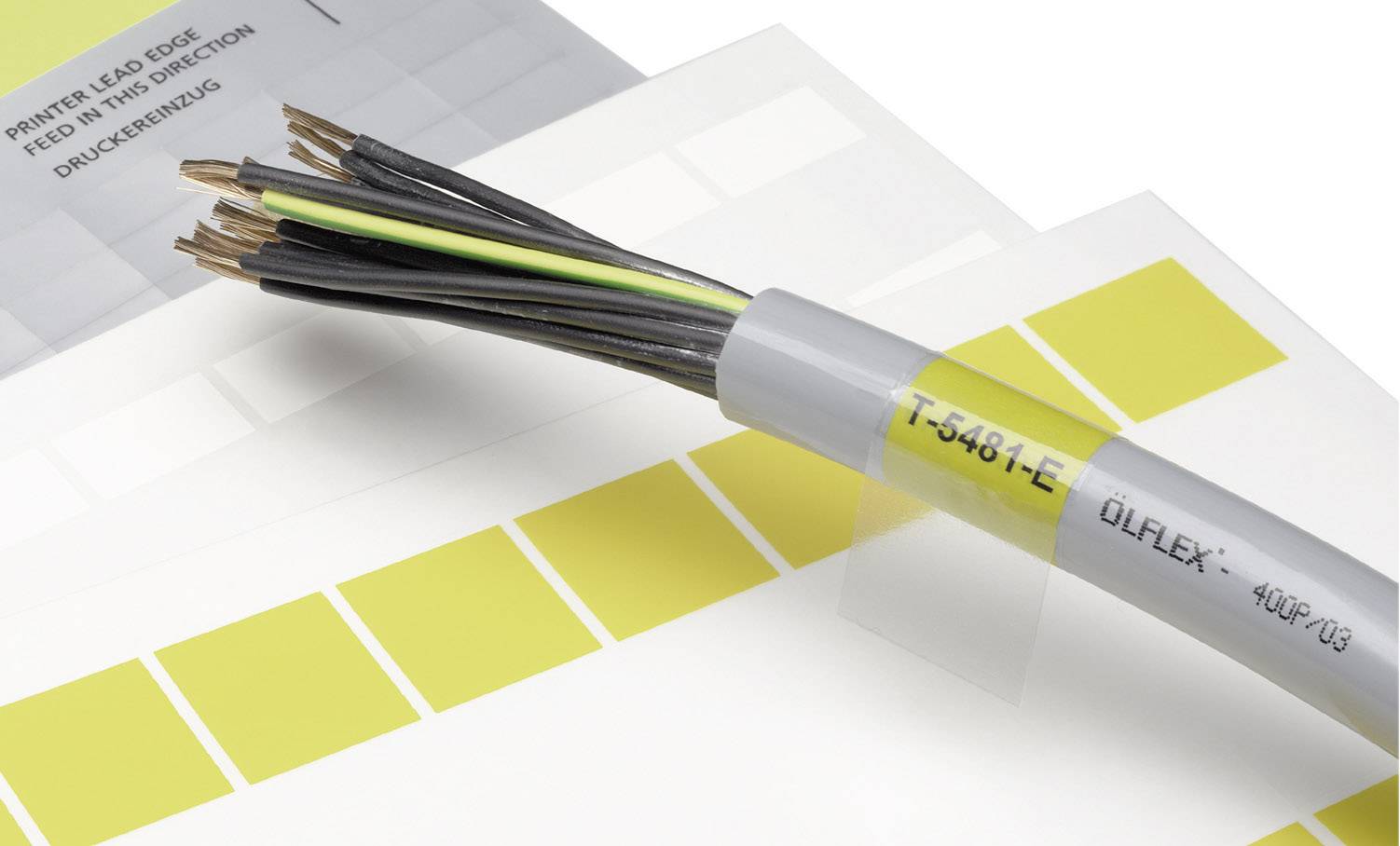 Ein graues Kabel mit offenen Kupferdrähten liegt auf Farbmustern. Das Kabel ist mit 'T-5481-E OLFLEX' beschriftet.