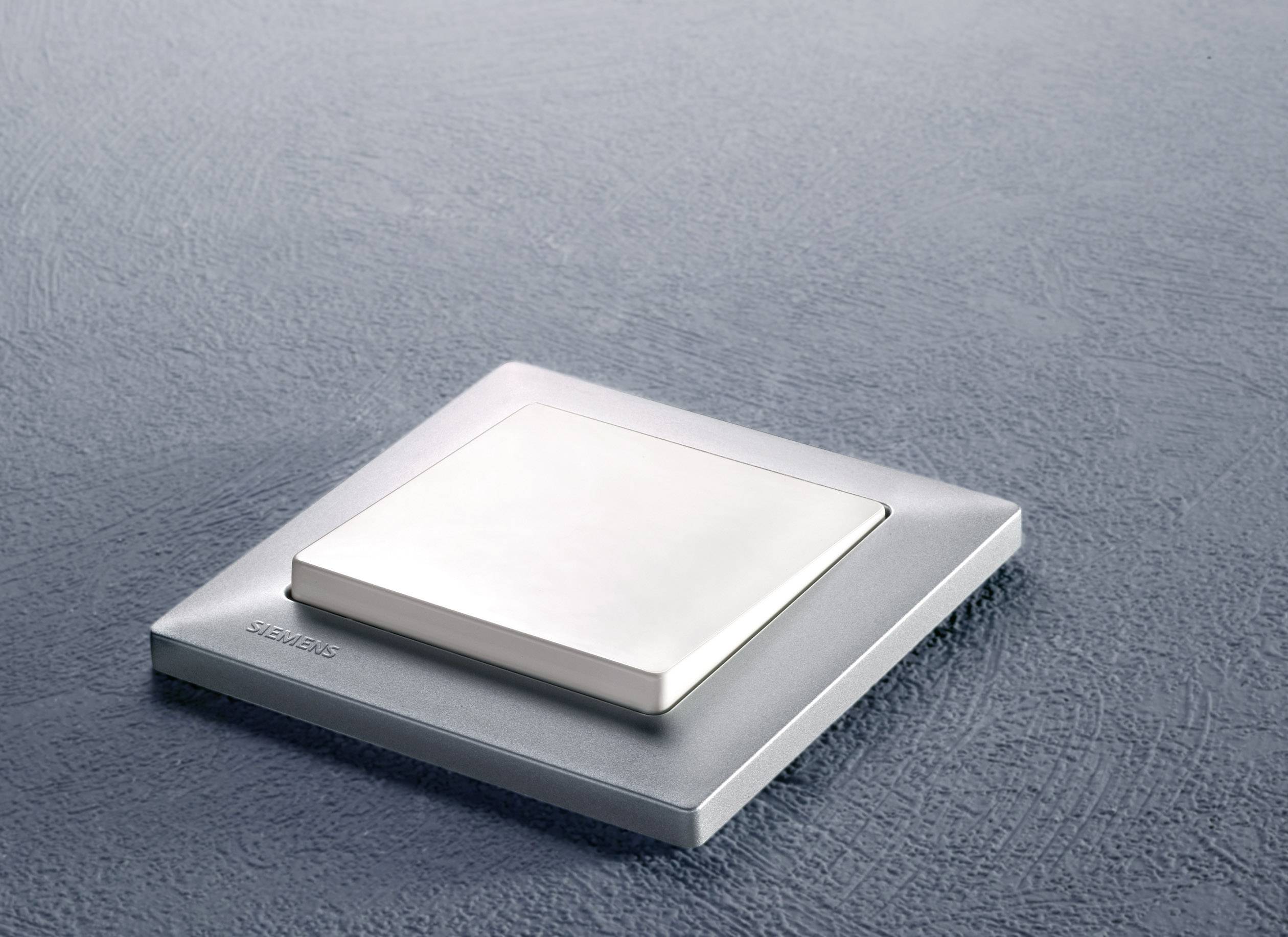 Ein eleganter, quadratischer Lichtschalter aus Metall mit flacher Oberfläche, montiert auf einer strukturierten, grauen Wand.