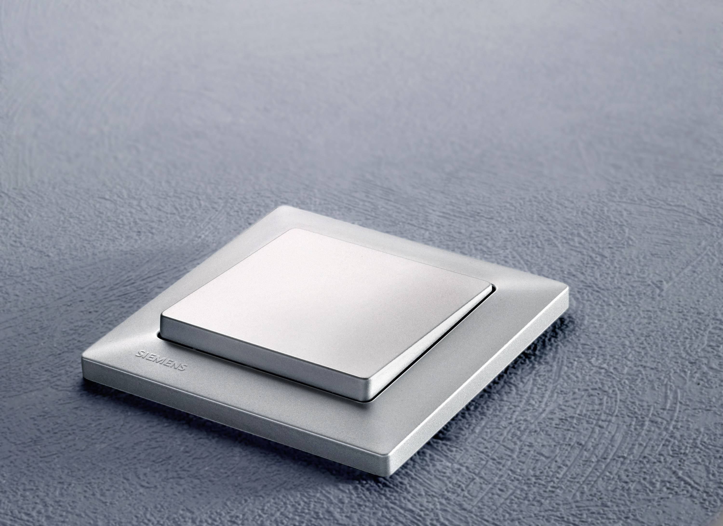 Ein moderner Lichtschalter aus gebürstetem Metall auf einer grauen Wand.