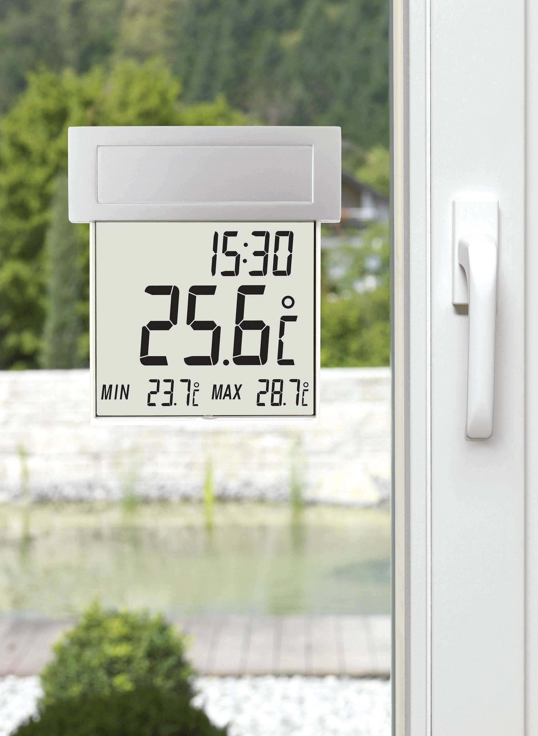 Digitales Thermometer am Fenster zeigt 15:30 Uhr und 25,6°C an, mit minimal 23,7°C und maximal 28,7°C. Hintergrund: Garten.