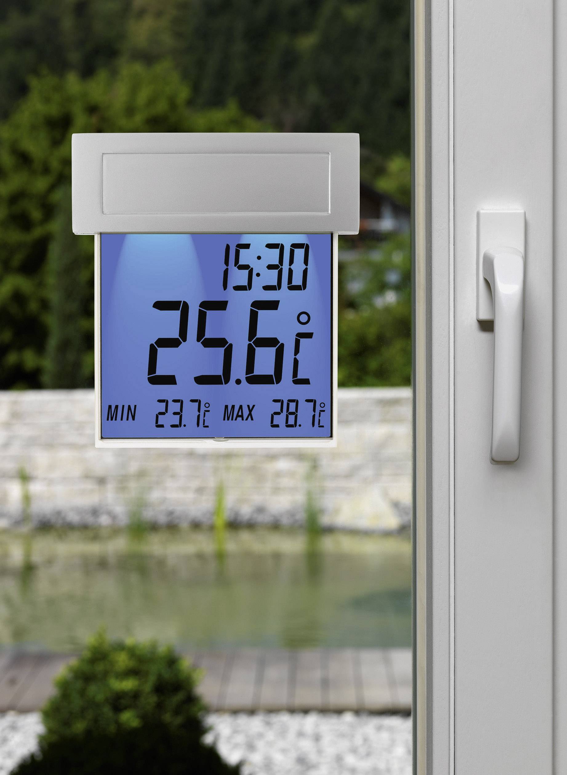 Digitales Thermometer zeigt 25,6°C um 15:30 Uhr an. Min 23,7°C, Max 28,7°C. Hintergrund: Garten mit Teich, Blick durch ein Fenster.