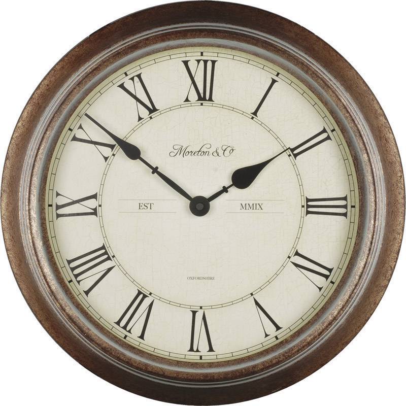 Runde Wanduhr mit römischen Ziffern und zwei Zeigern. Markiert mit 'Moreton & Co' und 'EST MMIX'. Holzrahmen und beiges Zifferblatt. Zeigt 10:10 Uhr.