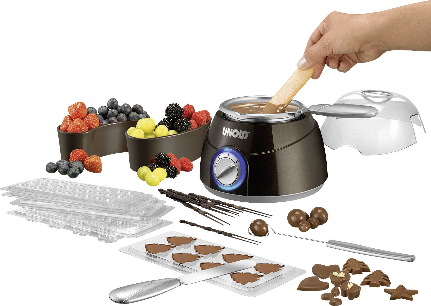 Eine Schokoladenschmelzmaschine mit Früchten, Schokoladenformen und -werkzeugen. Eine Hand rührt geschmolzene Schokolade um.