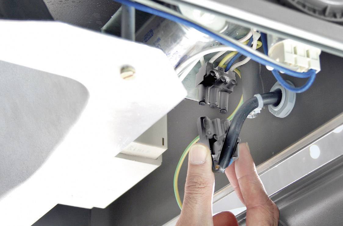 Person zeigt auf eine komplexe Verkabelung unter einem Gerät. Es sind mehrere Kabel und Anschlüsse sichtbar, die für Elektronik relevant sind.