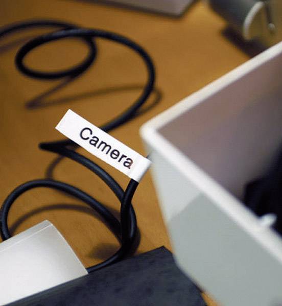 Ein Kabel mit einem Etikett, auf dem 'Camera' steht. Es liegt auf einem Tisch neben einer offenen weißen Schachtel.