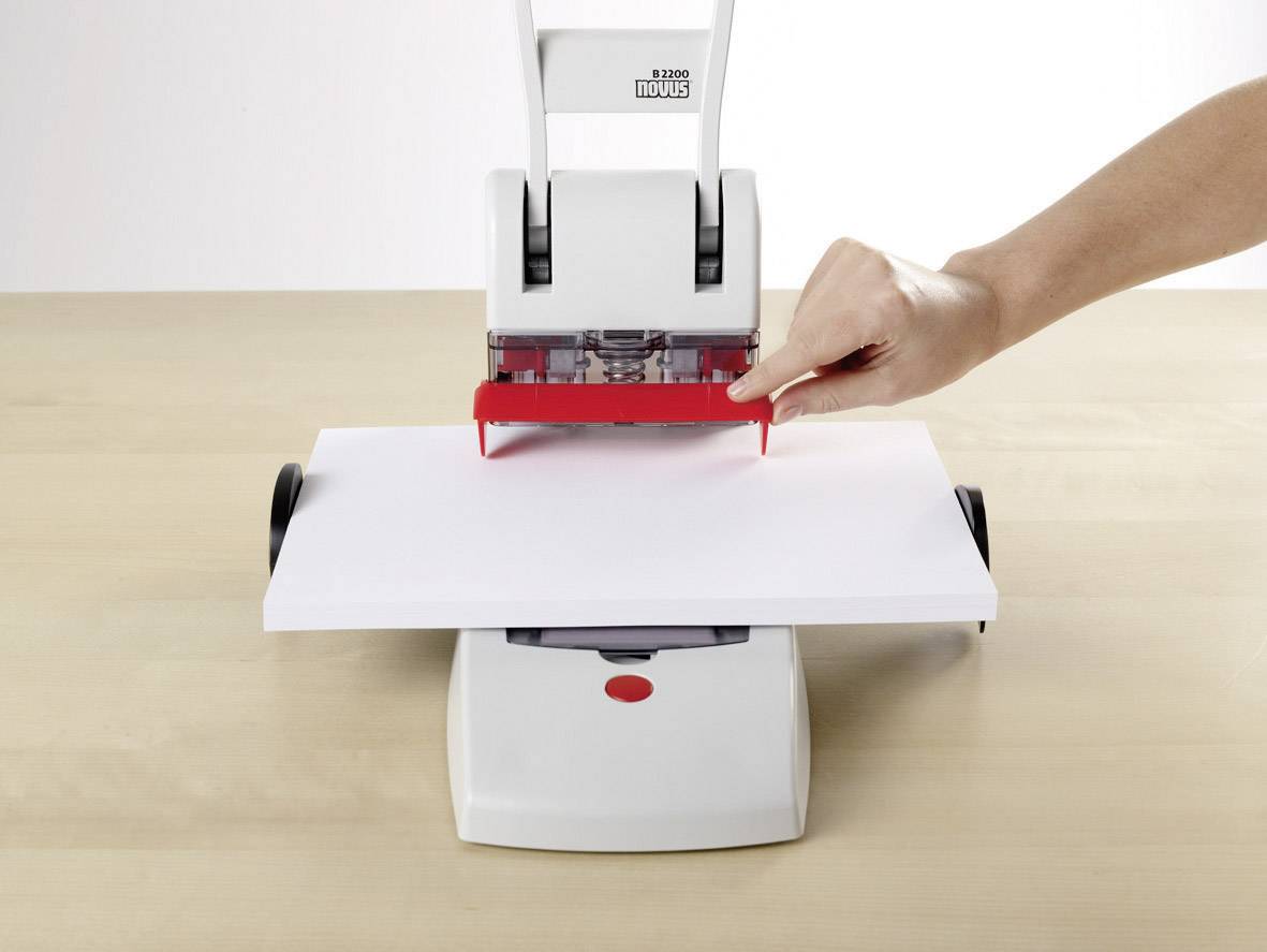 Eine Hand benutzt eine manuelle Maschine, um ein Blatt Papier auf einem Tisch zu perforieren.