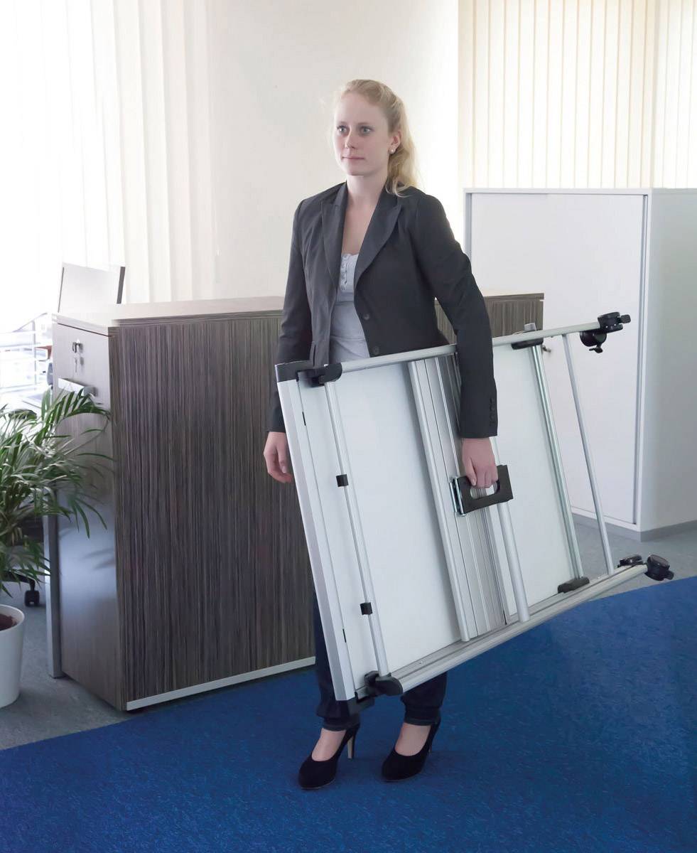 Eine Frau trägt eine zusammengeklappte Tafel in einem Büro. Im Hintergrund sind Pflanzen und Möbelstücke zu sehen.