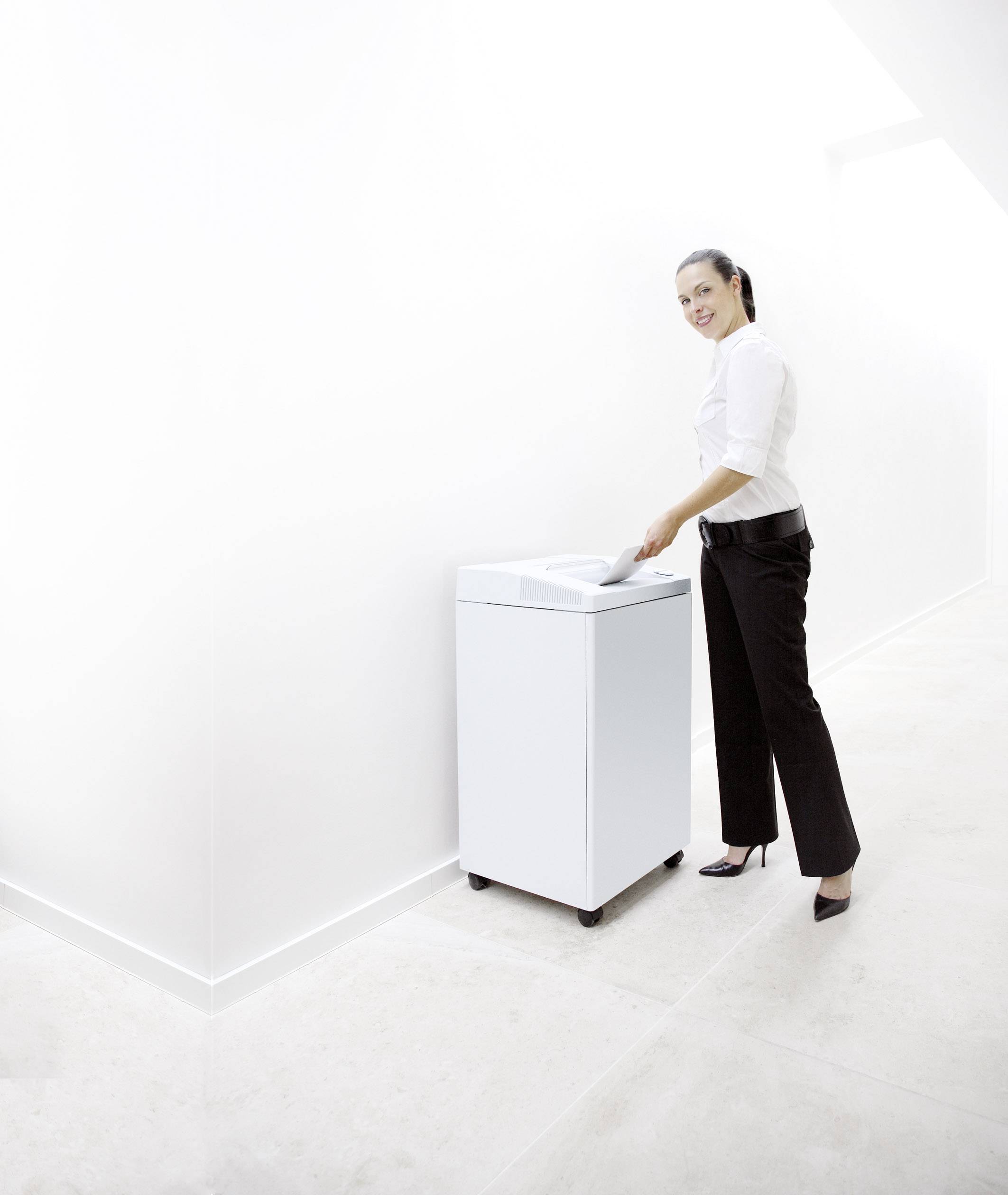 Frau entsorgt Papier in einen weißen Mülleimer auf Rädern in einem hellen, minimalistischen Raum.