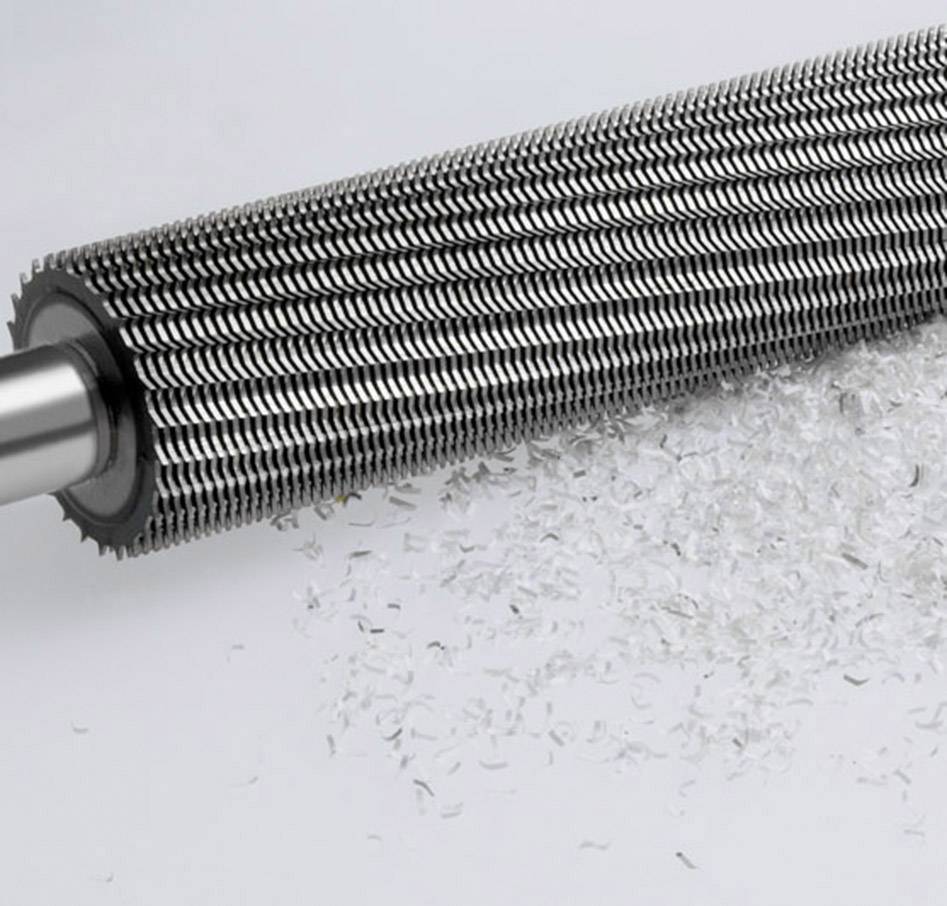 Eine große Metallrolle mit scharfen Klingen, die weiße Plastikspäne zersetzt.