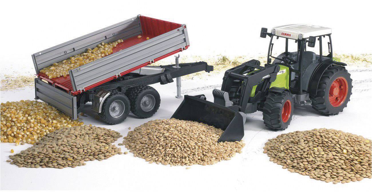 Ein Traktor mit Anhänger entlädt Getreide auf den Boden. Großer Haufen von Mais und anderen Körnern zu sehen.