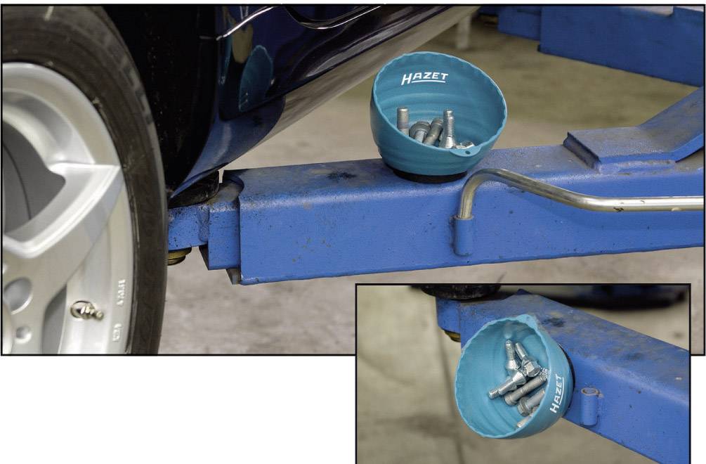 Ein blaues Gefäß von Hazet hält Schrauben und liegt auf einem Fahrzeugheber, nahe einem Autoreifen.