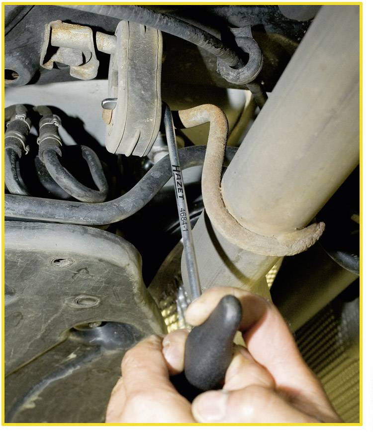 Eine Person verwendet ein Werkzeug, um an einem Teil unter einem Fahrzeug zu arbeiten. Im Fokus ist die Hand mit einem Schraubenschlüssel.