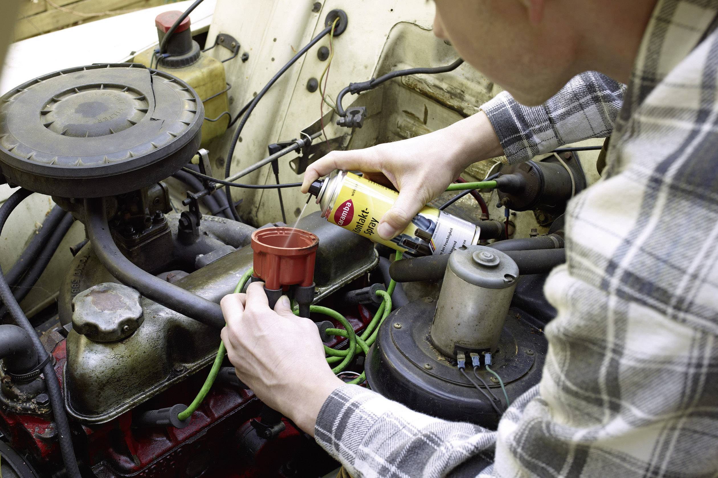 Eine Person sprüht Wartungsmittel auf den Motor eines Autos und konzentriert sich dabei auf die Zündverteilerkappe.
