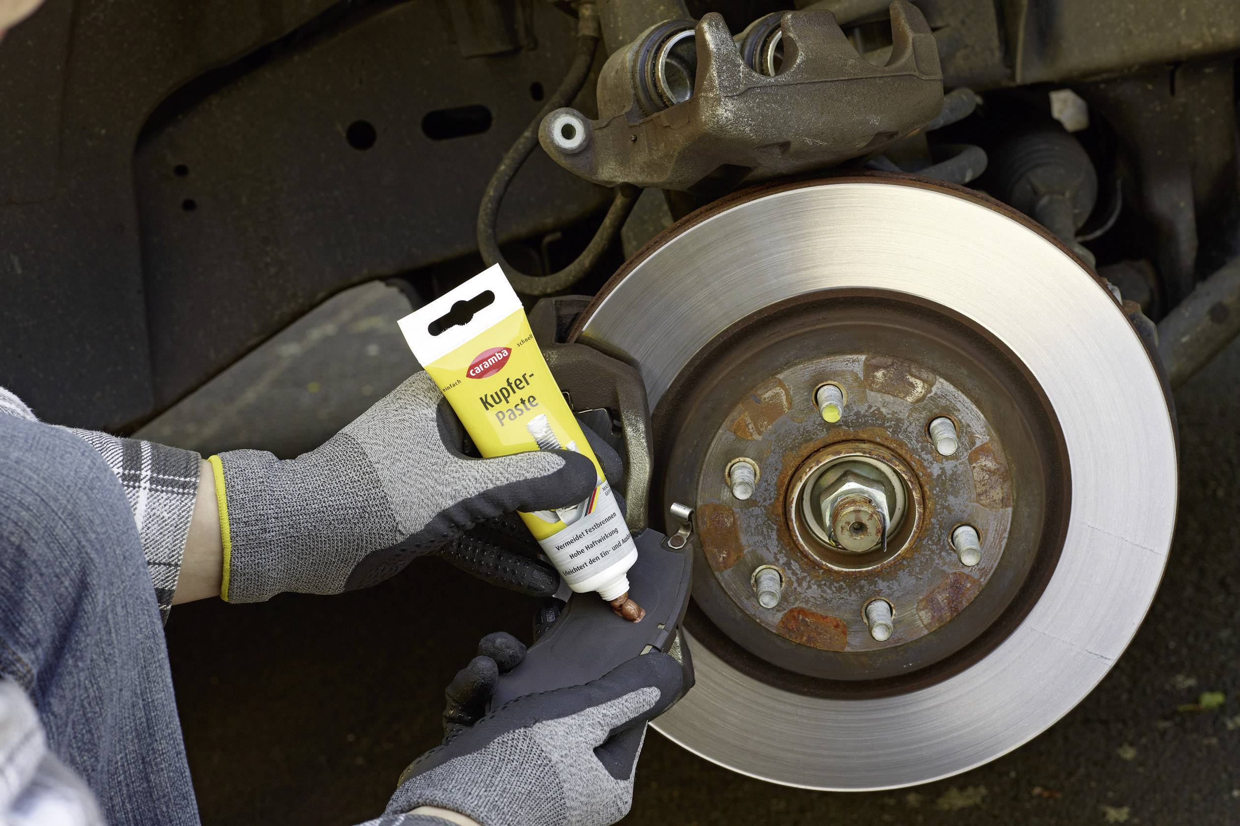 Eine Person trägt Kupferpaste auf die Rückseite eines neuen Bremssattels auf, der an einer Auto-Bremsscheibe montiert ist.