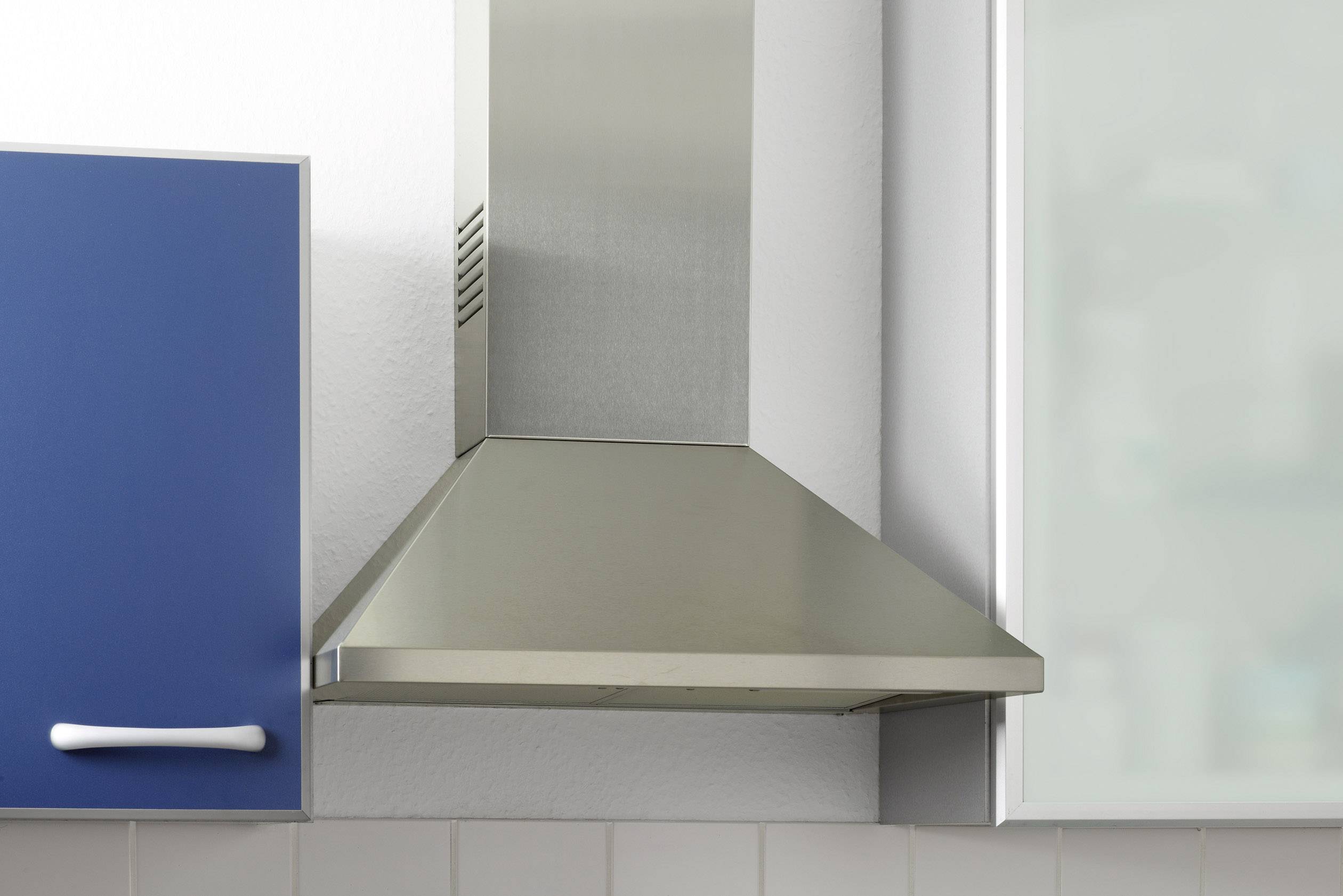 Eine Edelstahl-Dunstabzugshaube montiert zwischen einem blauen Schrank und einer verglasten Fläche in einer modernen Küche.