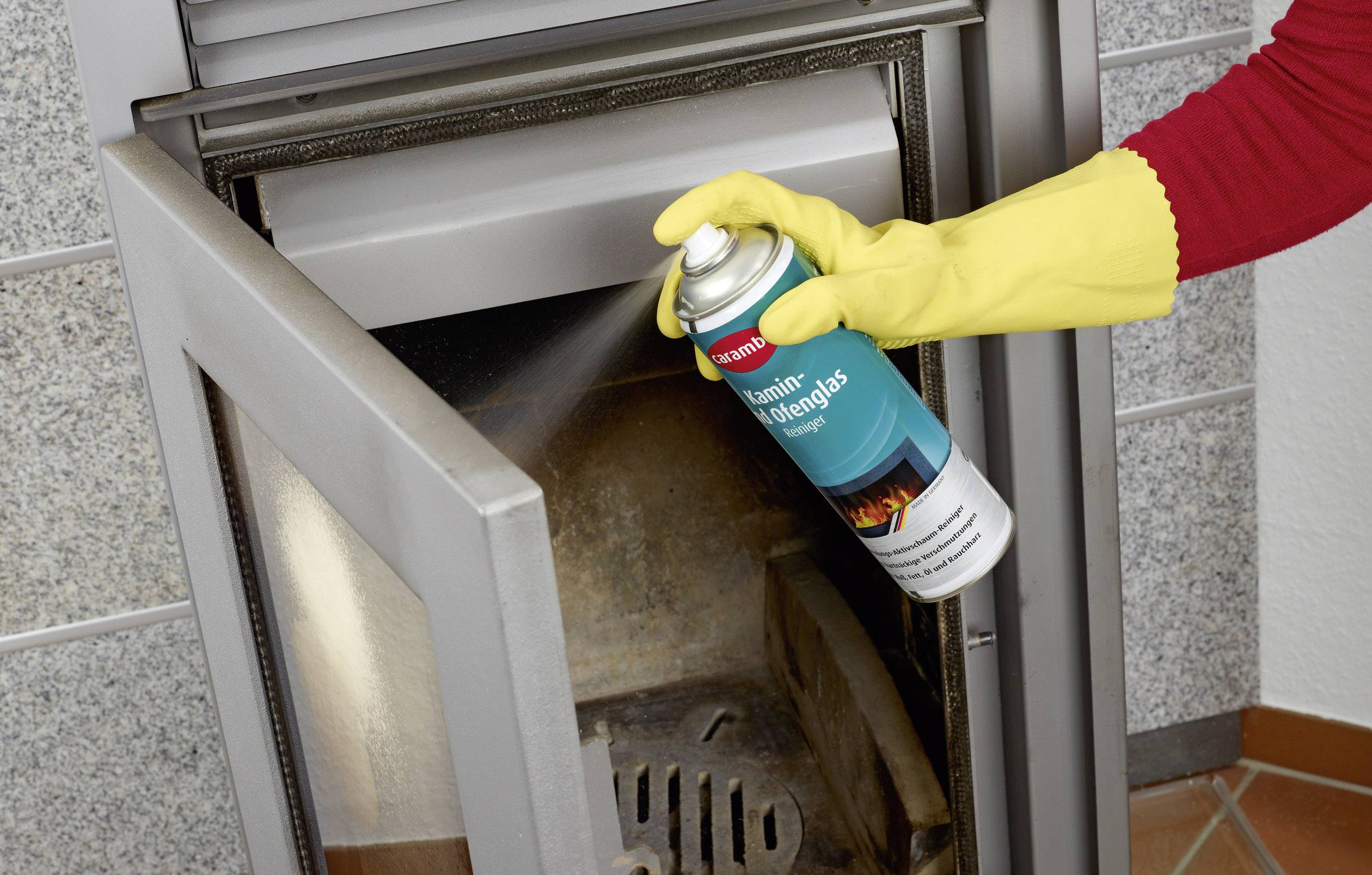 Eine Person mit gelbem Handschuh sprüht Kamin- und Ofenglasreiniger auf die Innenseite eines Ofentürglases.