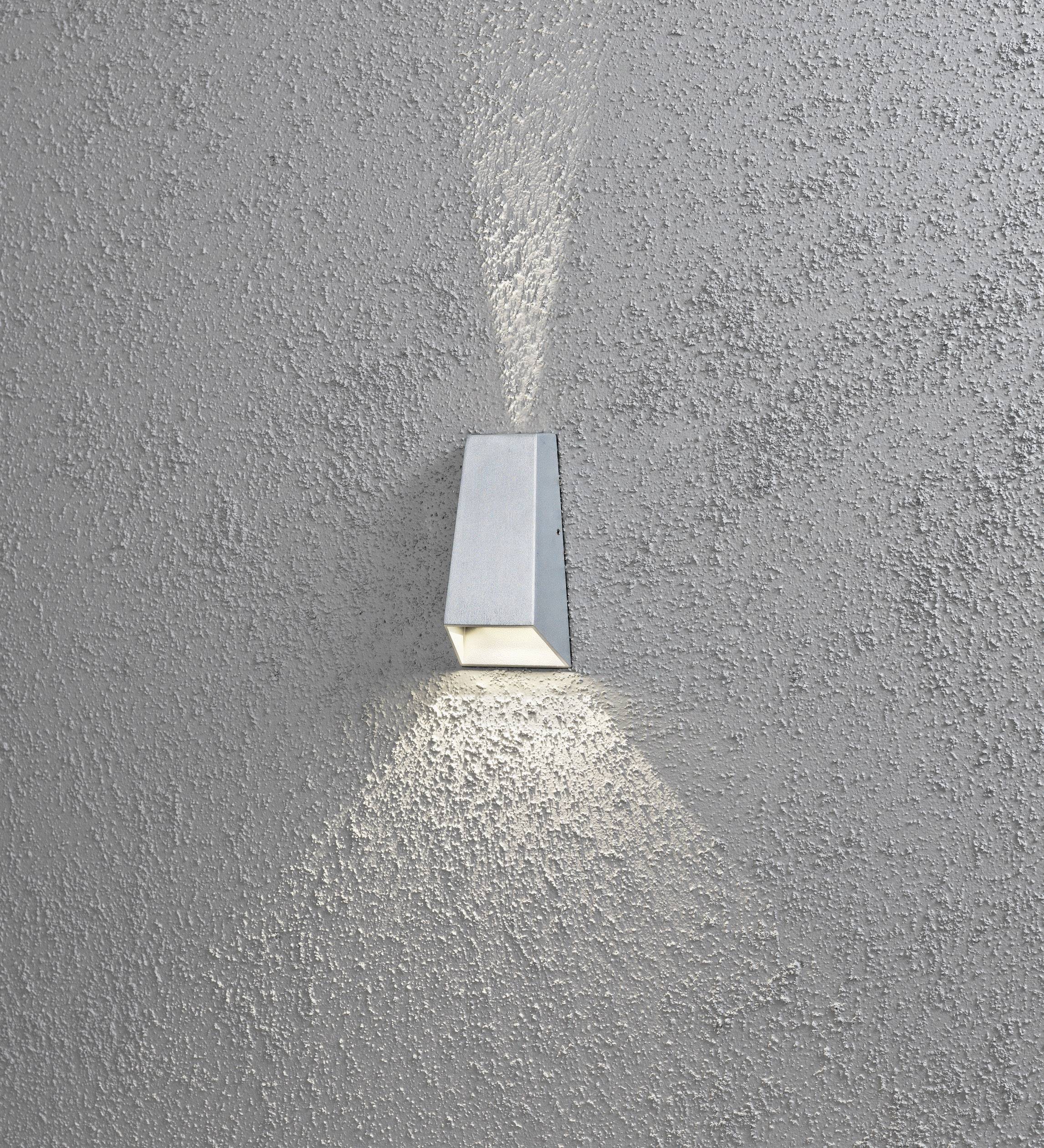 Eine moderne Wandleuchte aus Metall wirft Lichtstrahlen nach oben und unten auf eine strukturierte graue Wand.