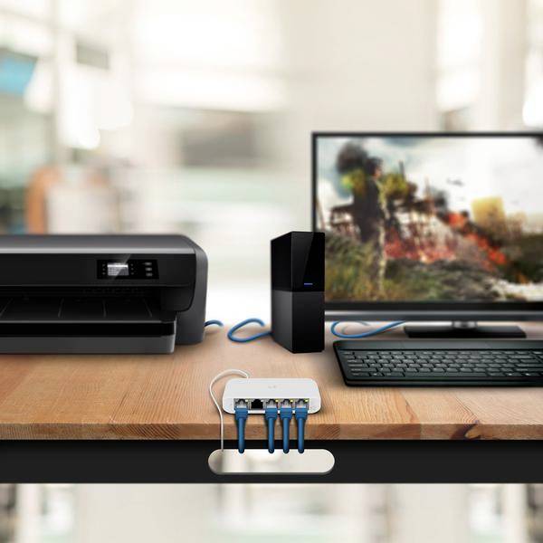 Ein Schreibtisch mit einem Drucker, einem Computerbildschirm, einer Tastatur und einem Router, verbunden über Kabel auf einer Holzoberfläche.