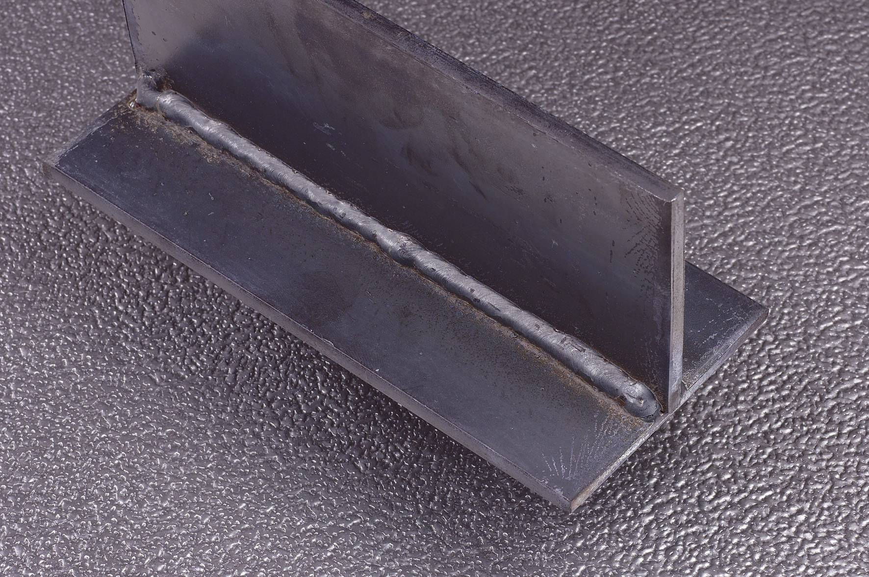 Ein Schweißnaht in einer Metallverbindung, L-förmig angeordnet, auf einer strukturierten, grauen Oberfläche.