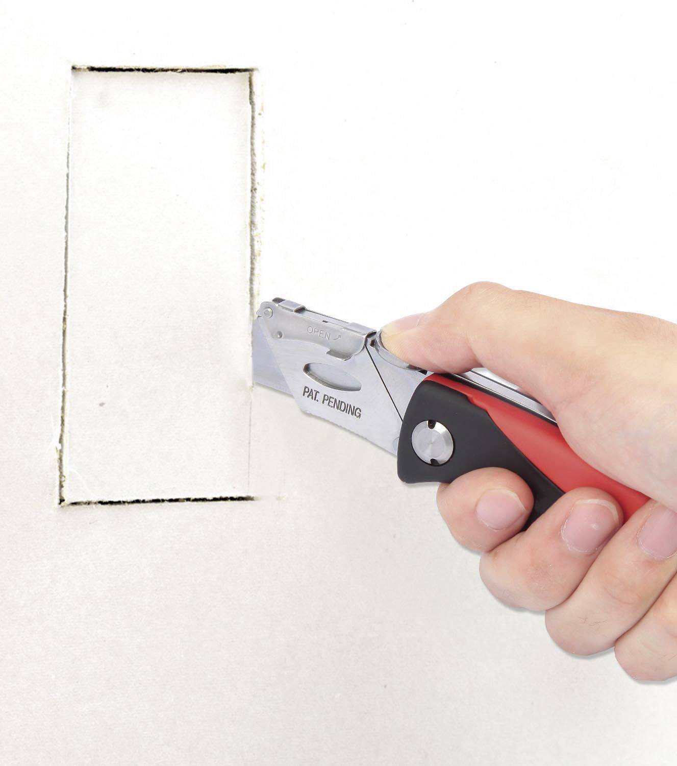 Eine Hand schneidet mit einem roten Teppichmesser ein rechteckiges Loch in die weiße Wand.