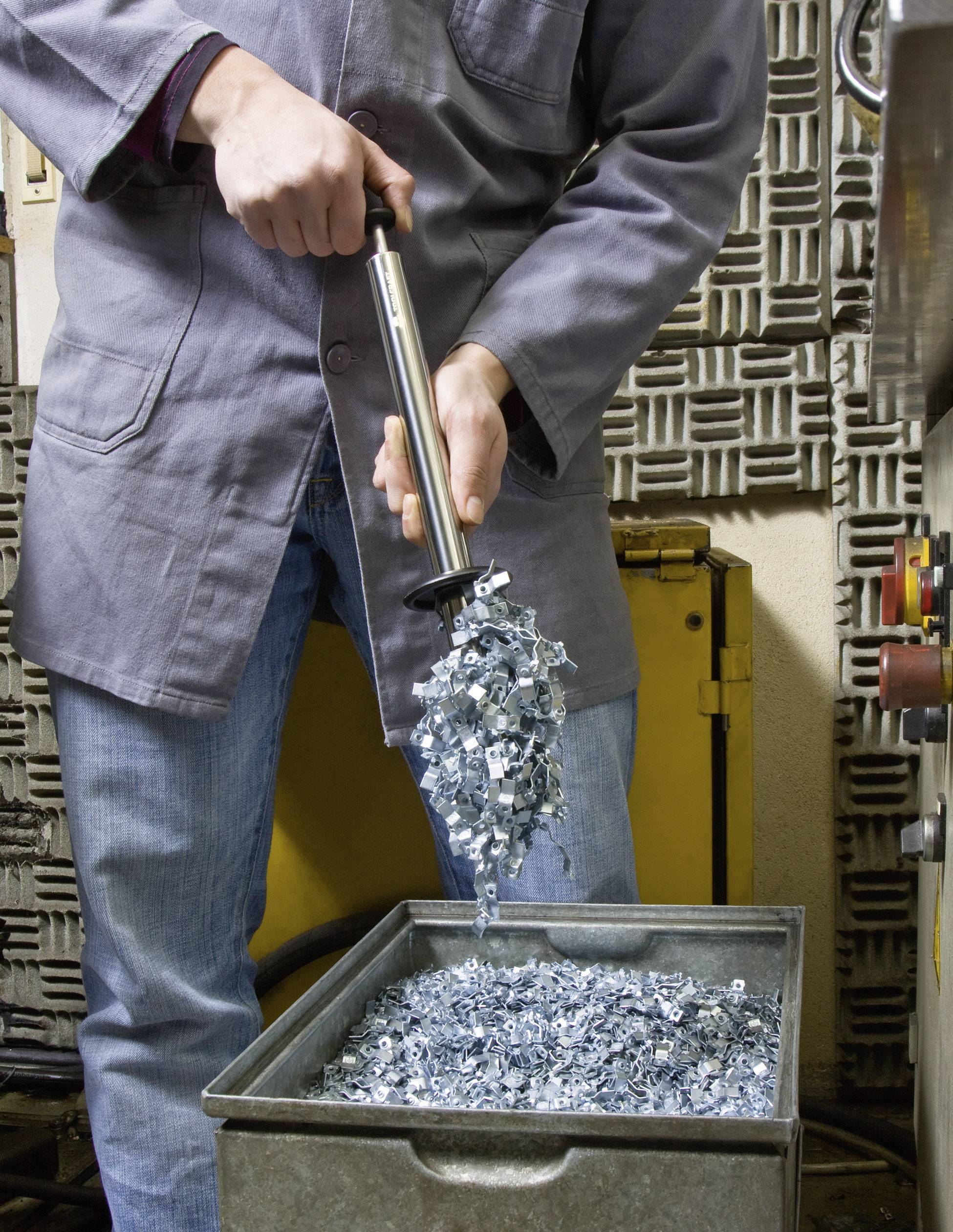 Ein Techniker in Schutzkleidung hält Metallteile mit einem Magnetstab über einen Behälter. Die Teile fallen vom Magneten in die Box.