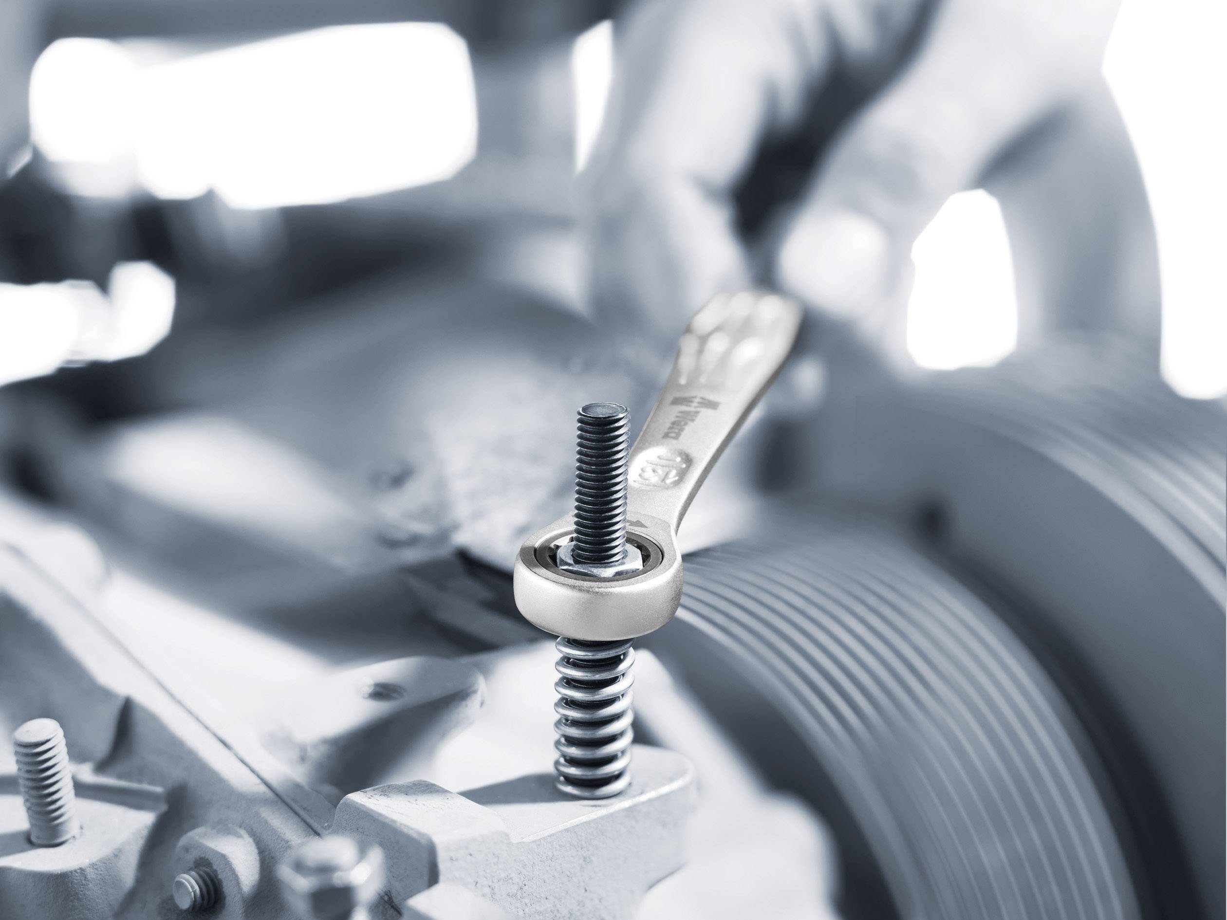 Eine Hand zieht eine Schraube mit einem Schraubenschlüssel an, zeigt präzise Mechanikarbeit an einer Maschine.