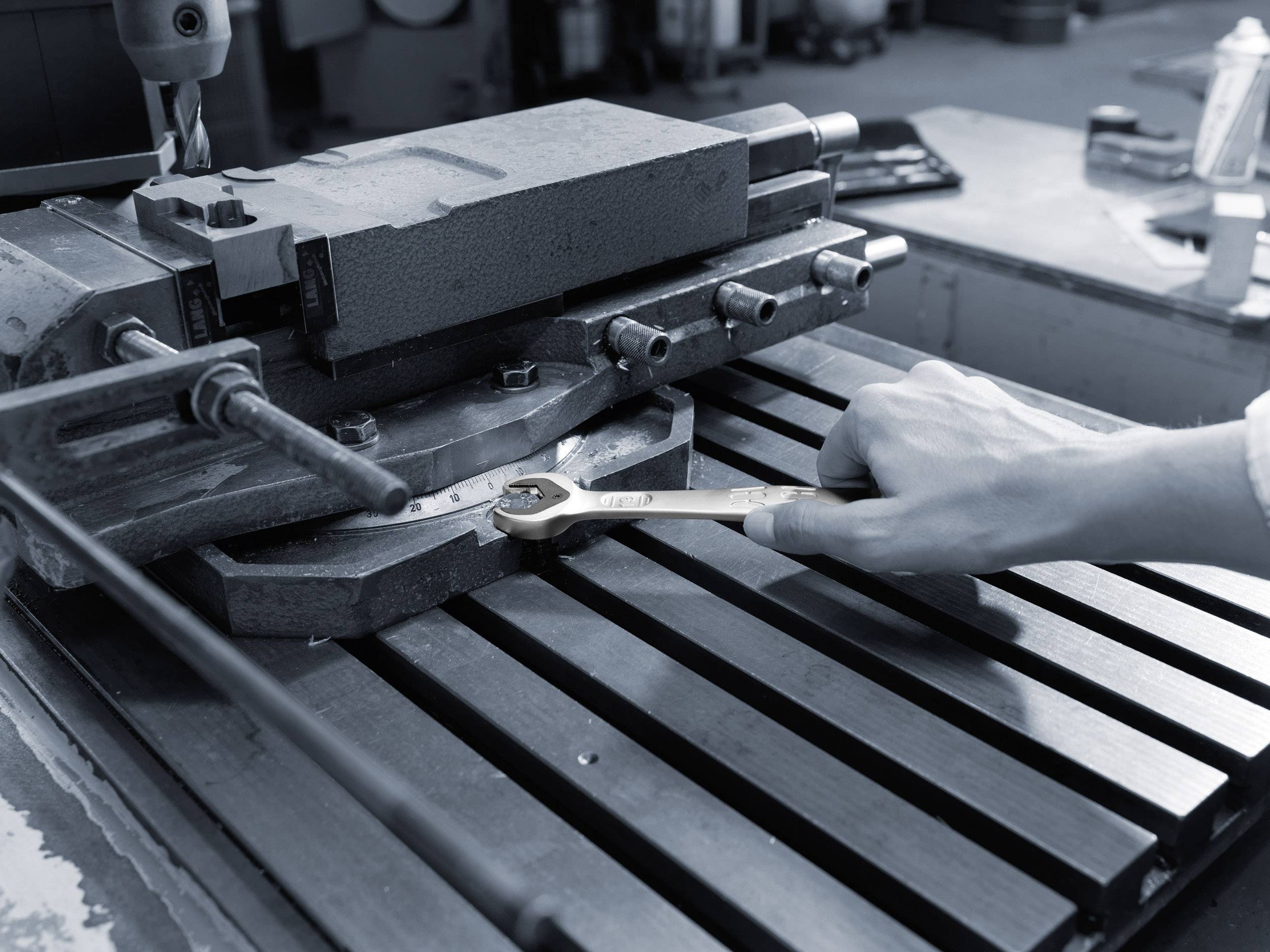 Eine Person arbeitet mit einem Schraubenschlüssel an einer Metallmaschine. Der Arbeitsplatz hat ein industrielles Ambiente.