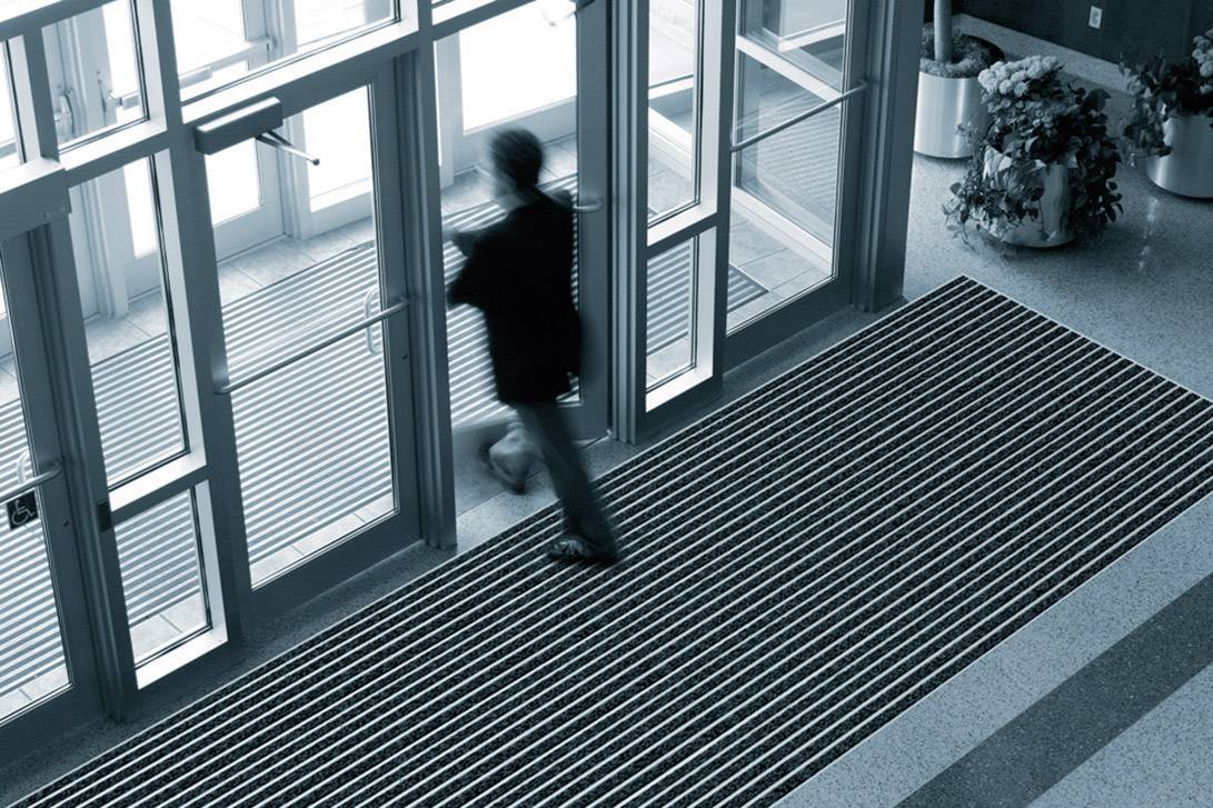 Eine Person verlässt durch eine Drehtür ein modernes Gebäude, beleuchtet von natürlichem Licht.