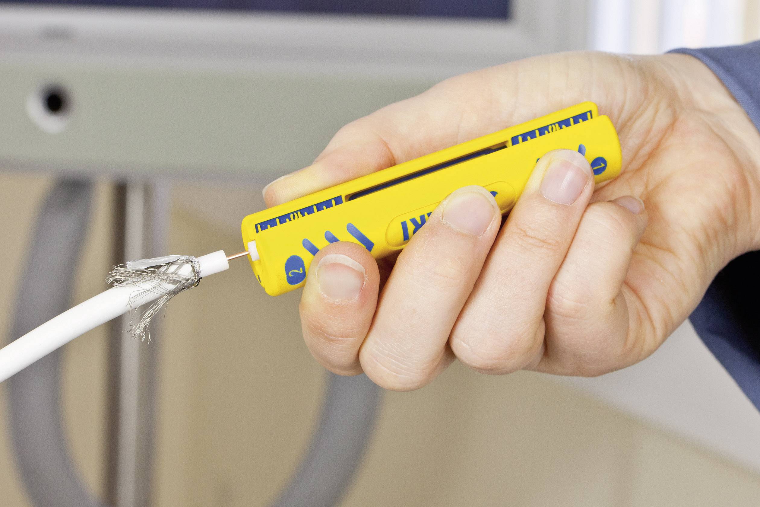 Eine Hand hält ein gelbes Kabeltestgerät gegen ein beschädigtes Stromkabel. Das Kabel hat freiliegende Drähte, was auf Gefahr hinweist.