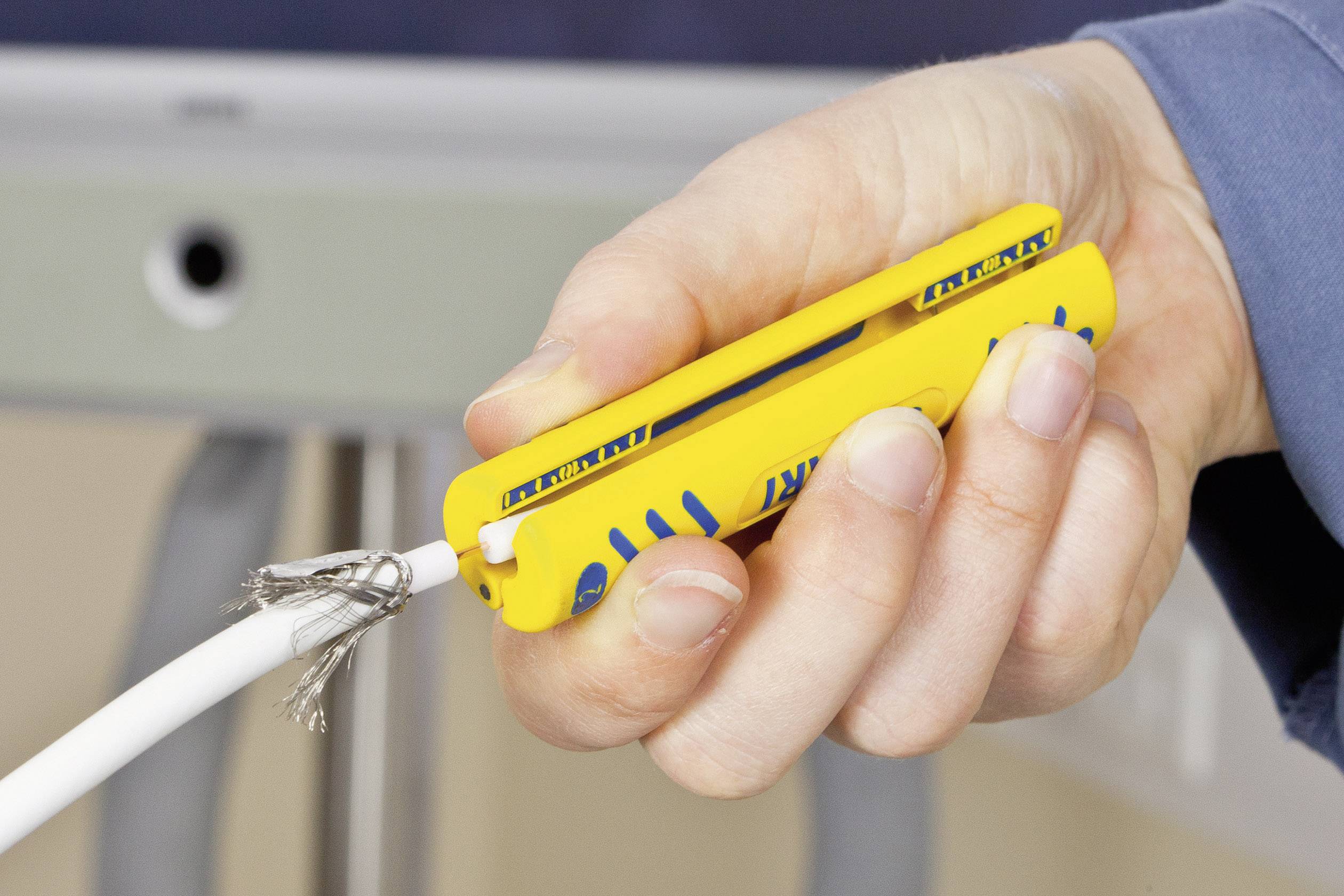 Eine Hand hält ein gelbes Kabelabziehwerkzeug, um die Isolierung eines weißen Kabels zu entfernen.